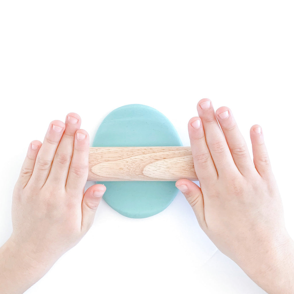 little hands using wooden rolling pin to roll out blue cotton candy scented dough